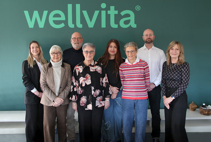 Group of people standing in front of a wellvita branded background