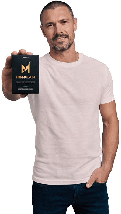 A man in a light pink t-shirt and dark jeans holds up a black box of 'wella' Formula M hair product against a solid white background.